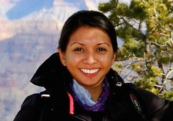 Lady with blackhair smiling at the camera stadning in front of Grand Canyon