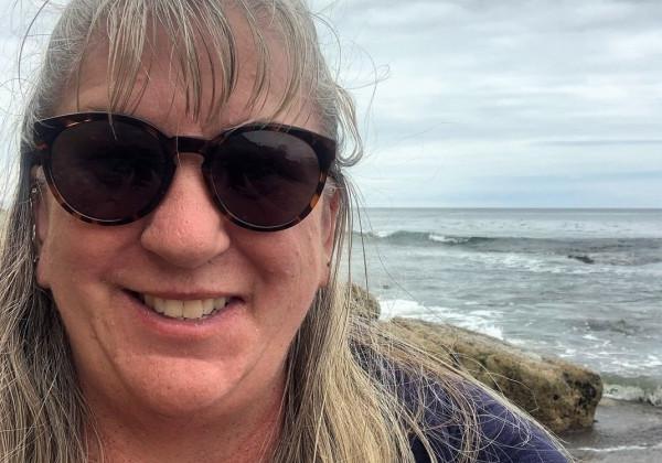 A woman at the beach wearing sunglasses and smiling. 