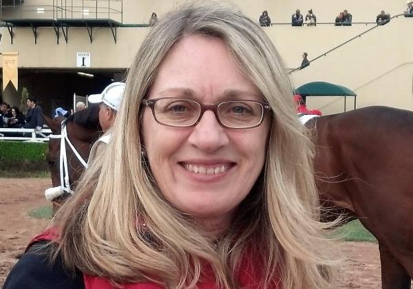 A woman at a horse track and smiling at the camera. 