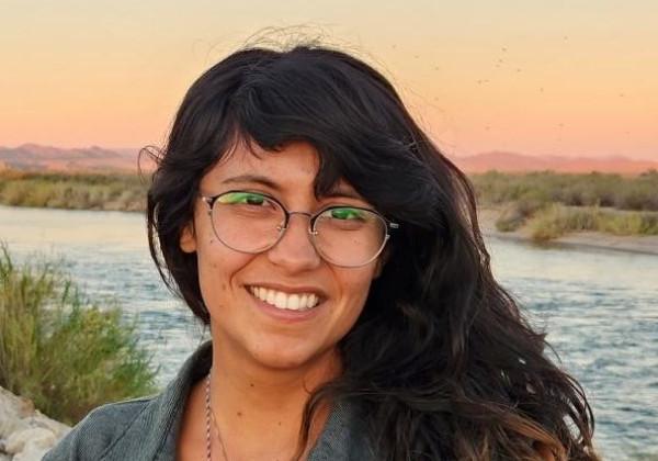 A woman with long hair standing in front of the a river smiling. 