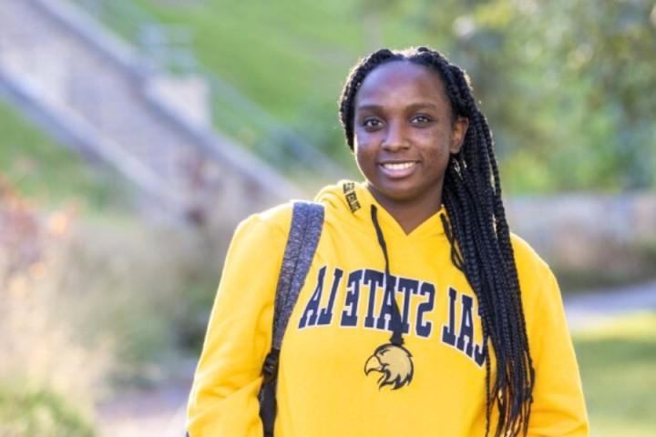 Student wearing yellow hoodie smiling with a backpack on.