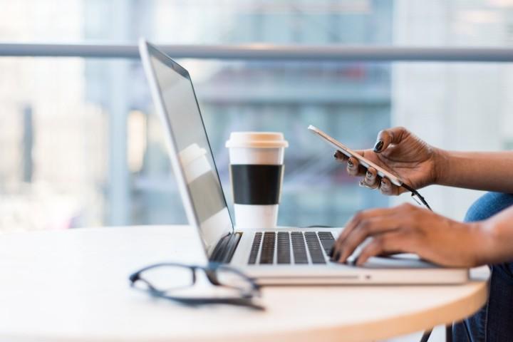 Womans hands holding a phone over  a laptop