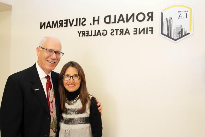 Two people smiling while standing in front of the Ronald H. Silverman Fine Arts Gallery