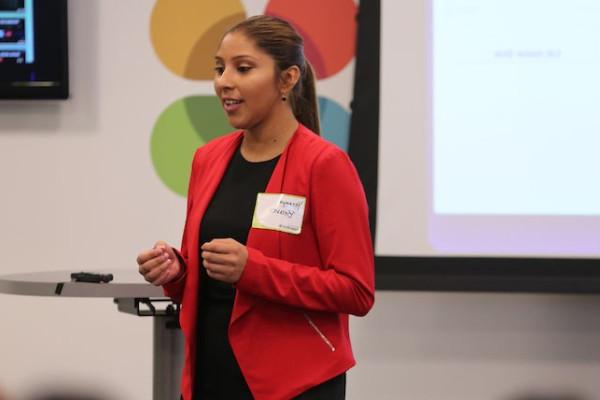 Image of a female student in a red blazer giving a presentation to her classmates. 