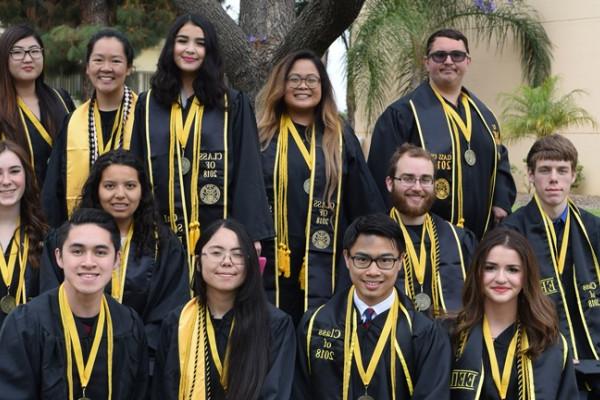 Group of Honors College graduating students in Commencement regalia, gathered in front of the jacaranda tree on campus. 