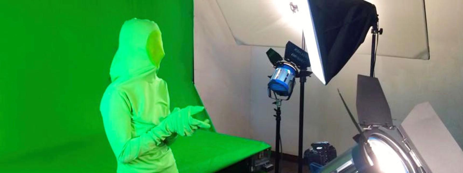 Image of a student in a green suit in front of a green screen being filmed. 