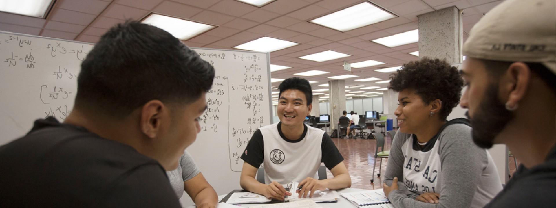 一群学生聚集在图书馆里，围着一块白板学习. 